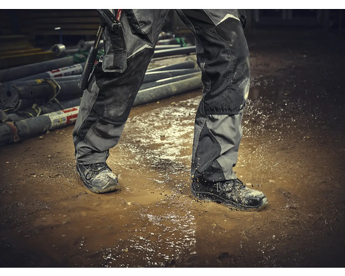 Osoba v pracovných nohaviciach a bezpečnostnej obuvi stojí v kaluži.