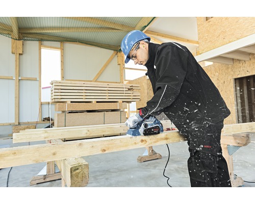 Remeselník hoblí drevenú dosku elektrickým hoblíkom v dielni.