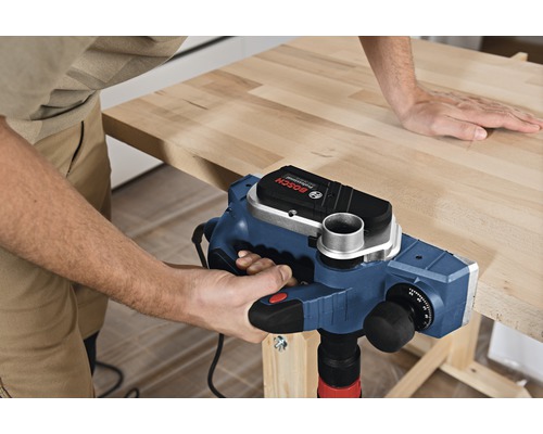 Remeselník opracováva obrobok elektrickým hoblíkom. Logo Bosch.