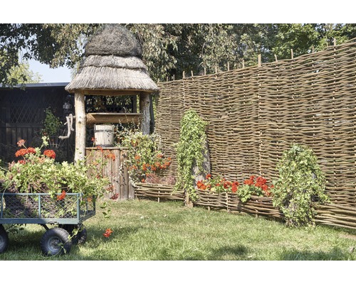 Scéna so záhradnou studňou, prúteným plotom, kvetinovým vozíkom a osadenými prútenými debničkami