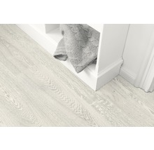 Svetlá drevená podlaha vedľa bielej police so sivou dekou.