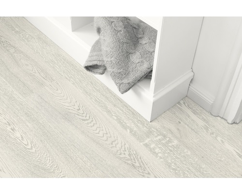 Svetlá drevená podlaha vedľa bielej police so sivou dekou.