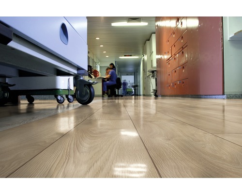 Svetlá drevená podlaha na chodbe nemocnice s lekárskym vybavením a personálom