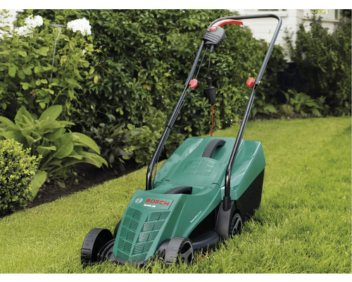 Elektrická kosačka na trávu na trávniku pred kríkmi