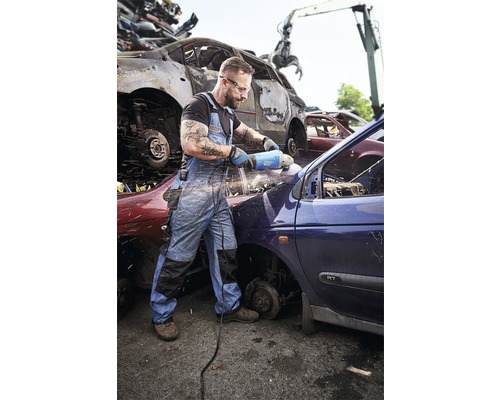 Muž pracuje s brúskou na aute na vrakovisku.