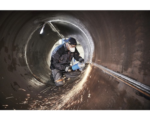 Pracovník používa uhlovú brúsku vo veľkej rúrke, z ktorej odlietajú iskry.