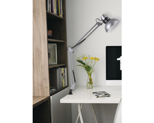 Stôl s otočnou lampou, počítačom, zápisníkom a kyticou pred knižnicou.