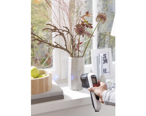 Scéna s infračerveným teplomerom používaným na okennom parapete pred oknom.