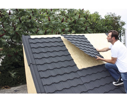 Muž pokladá kovové strešné tašky na strechu.