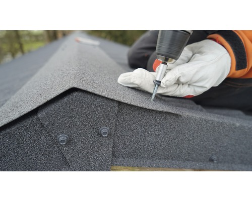 Osoba pripevňuje strešné šindle skrutkovačom.