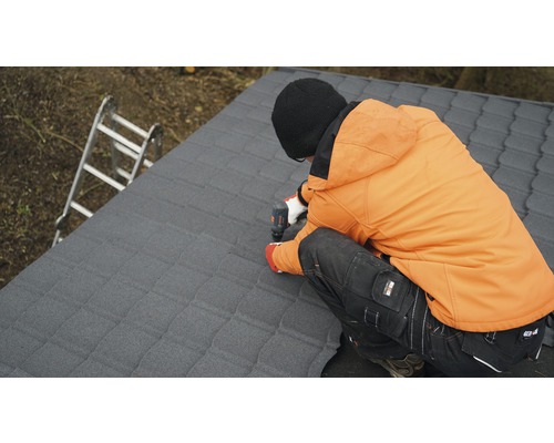 Remeselník pripevňuje strešné tašky akumulátorovým skrutkovačom na strechu