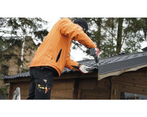 Remeselník montuje strešnú lepenku na záhradný domček pomocou akumulátorového skrutkovača.