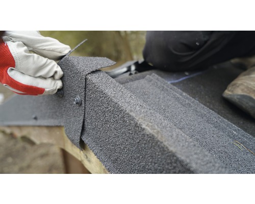 Detailný záber inštalácie strešných šindľov pomocou skrutiek osobou v rukaviciach.