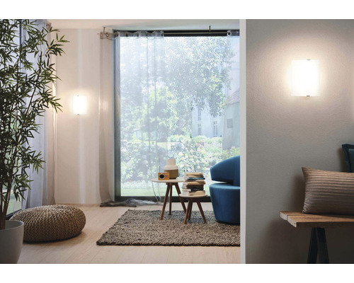 Obývacia izba s nástennými svietidlami, oknami so závesmi, príručnými stolíkmi a dekoratívnymi prvkami.