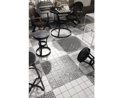 Scéna so šachovnicou na stole, stoličkami a zdobenými podlahovými dlaždicami