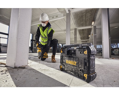 Stavebný robotník vŕta vŕtačkou v budove, vedľa neho nabíjačka Dewalt.