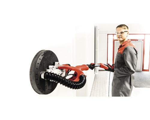 Muž brúsi stenu s brúskou na sadrokartón