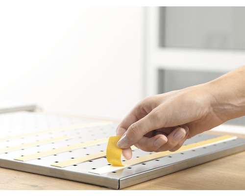 Osoba pripevňuje lepiace pásiky na dierovanú dosku.