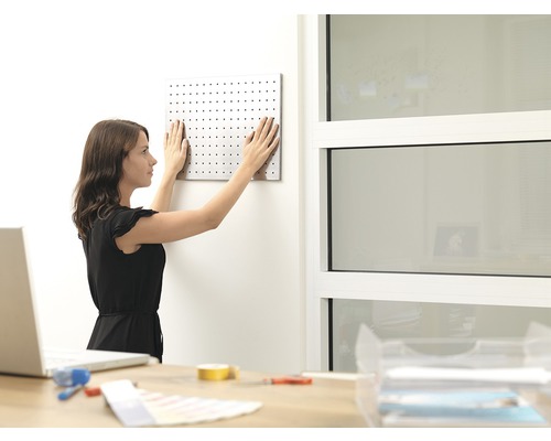 Žena pripevňuje dierovanú dosku na stenu v pracovni