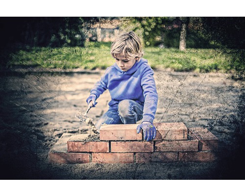 Chlapec stavia múr z tehál a lyžice