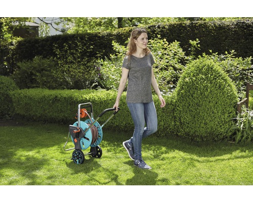 Žena ťahá vozík na záhradnú hadicu po trávniku.