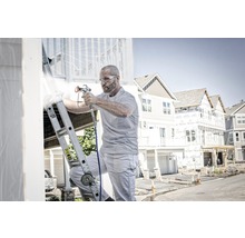 Muž na rebríku natiera dom striekacou pištoľou