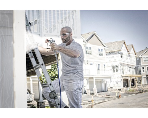 Muž na rebríku natiera dom striekacou pištoľou