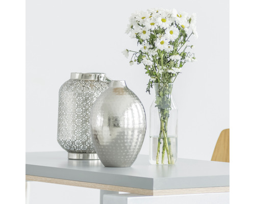 Dekoratívna scéna s lampášom, vázou a kyticou na stole.