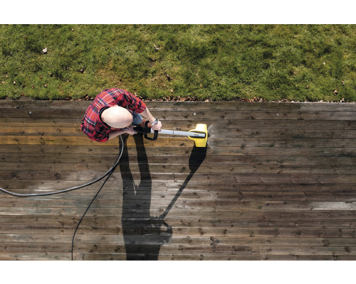 Osoba čistí drevenú terasu vysokotlakovým čističom