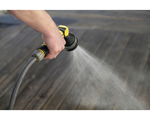Osoba zavlažuje drevenú podlahu záhradnou hadicou a striekacou pištoľou