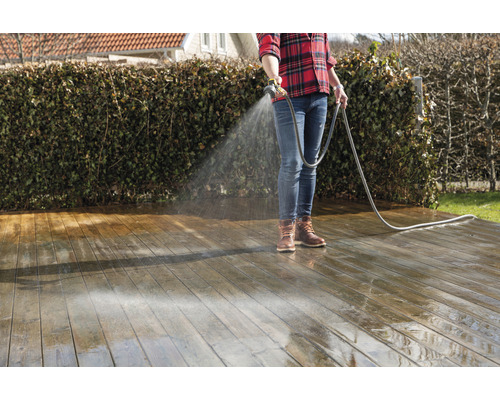 Osoba čistí drevenú terasu pomocou záhradnej hadice.