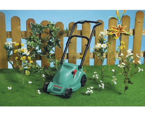 Kosačka na trávu Bosch na trávniku pred dreveným plotom a kvetmi
