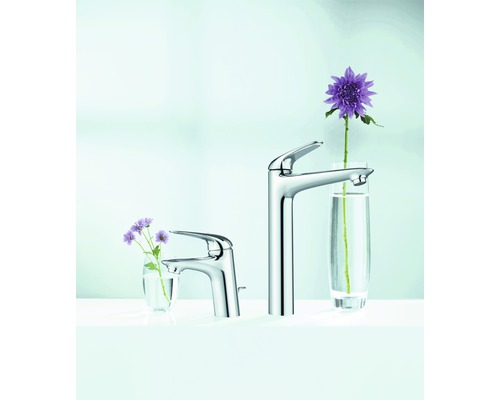 Dve umývadlové batérie z kovu rôznych veľkostí s kvetmi v pohároch.