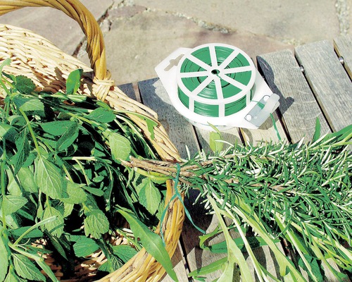 Viazací drôt a košík s čerstvými bylinkami na drevenom stole