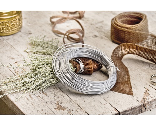 Dekoračná scéna s viazacím drôtom, jutovou stuhou a zelenými vetvami na drevenom stole