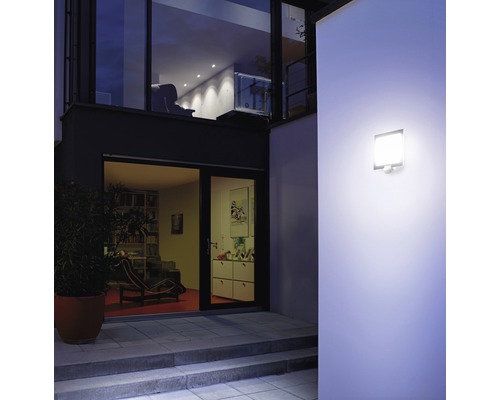 Osvetlená stena domu s vonkajšou lampou s pohybovým senzorom na príjazdovej ceste