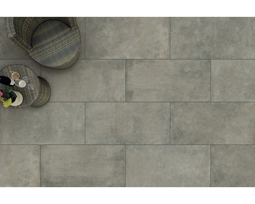 Pohľad na podlahu so sivými terasovými dlaždicami, ratanovým kreslom a malým stolíkom