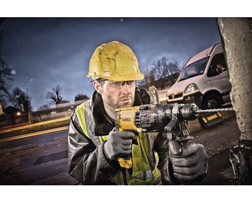 Stavebný robotník s ochrannou helmou vŕta vŕtačkou do objektu vonku.