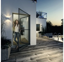 Vonkajší pohľad na dom so ženou stojacou v otvorených dverách s ochranou proti hmyzu, s výhľadom na terasu a bazén.