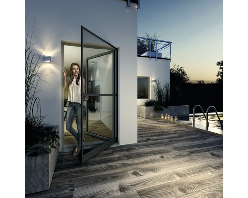 Vonkajší pohľad na dom so ženou stojacou v otvorených dverách s ochranou proti hmyzu, s výhľadom na terasu a bazén.