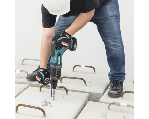 Muž vŕta akumulátorovým vŕtacím kladivom do betónových dosiek.