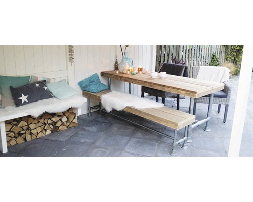 Drevený stôl a lavica s vankúšmi a dekoráciami v záhradnej časti