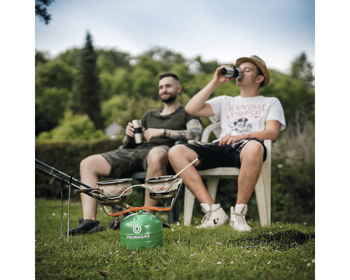 Dvaja muži sedia v záhrade vedľa kempingového variča Primagas s dvoma hrncami.