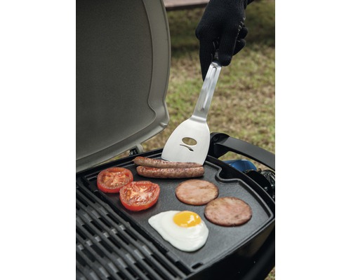 Gril s klobásami, paradajkami, slaninou a volským okom a osobou s obracačkou