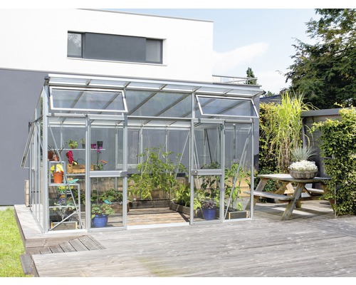 Skleník s rastlinami na drevenej terase pred domom.