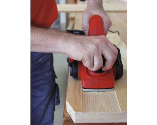 Osoba hoblí drevenú dosku elektrickým hoblíkom.