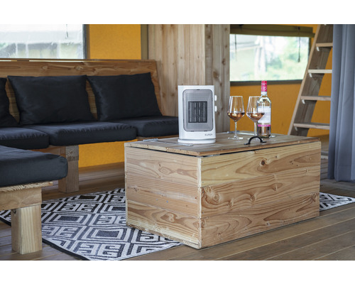 Interiérový pohľad s ventilátorovým ohrievačom, fľašou vína a pohármi na víno na drevenom stole vedľa posedenia