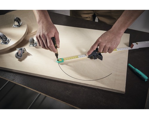 Osoba kreslí kružidlom a perom polkruh na drevenú dosku. Na doske sú aj nábytkové kolieska.