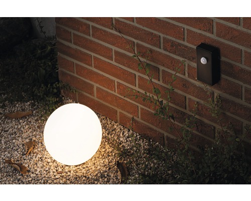 Scéna s okrúhlym vonkajším svietidlom a pohybovým senzorom na tehlovej stene