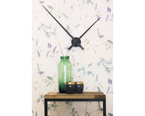 Dekorácia s nástennými hodinami, sklenenou vázou a sviečkami na drevenom stole pred kvetinovou tapetou